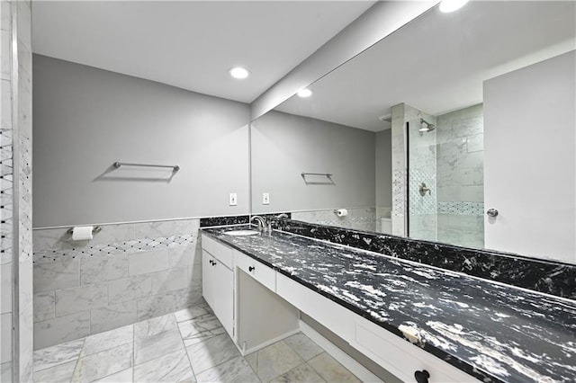 full bath featuring vanity, marble finish floor, walk in shower, recessed lighting, and a wainscoted wall