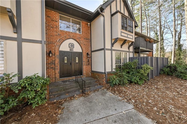 view of exterior entry featuring fence and brick siding