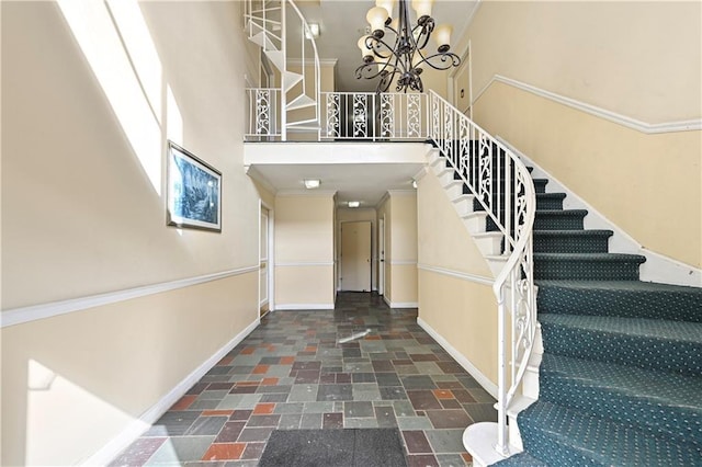 stairway featuring stone tile flooring, baseboards, crown molding, and a notable chandelier