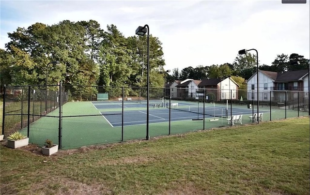 view of tennis court featuring fence and a yard