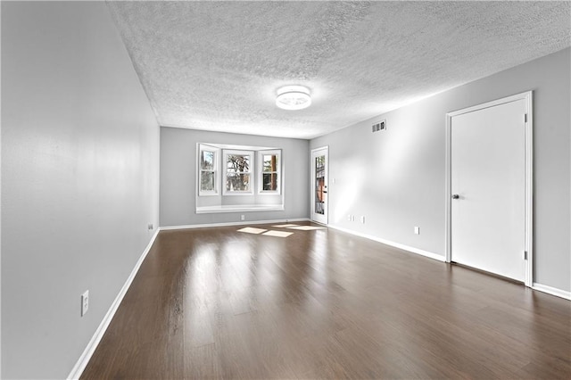 unfurnished living room featuring a textured ceiling, baseboards, visible vents, and wood finished floors