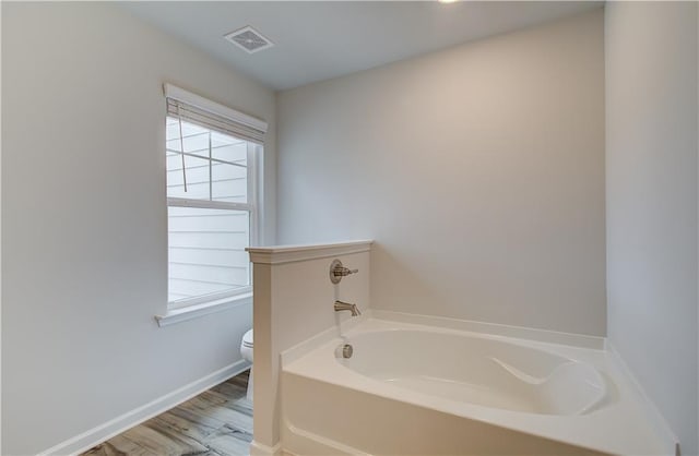 bathroom with wood-type flooring, a tub, and toilet