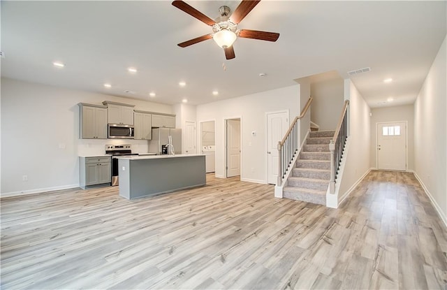 kitchen featuring gray cabinets, a kitchen island with sink, ceiling fan, stainless steel appliances, and light wood-type flooring