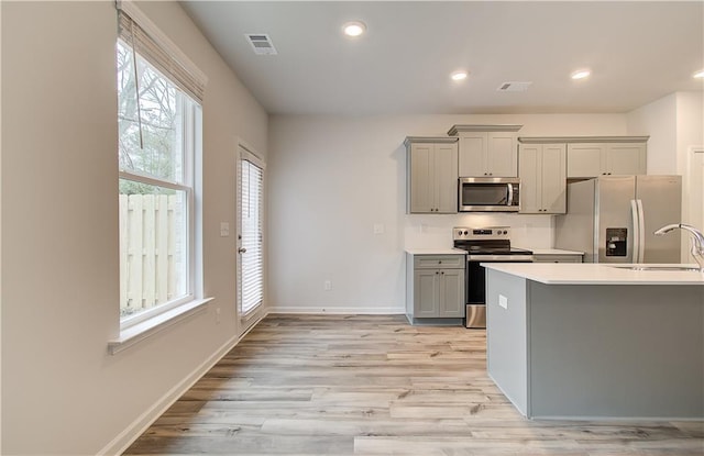 kitchen with gray cabinets, appliances with stainless steel finishes, sink, and light hardwood / wood-style flooring