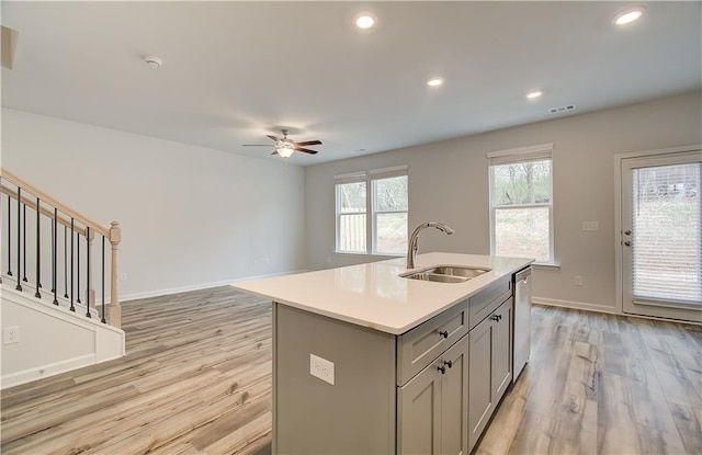 kitchen featuring sink, light hardwood / wood-style flooring, gray cabinets, a center island with sink, and stainless steel dishwasher