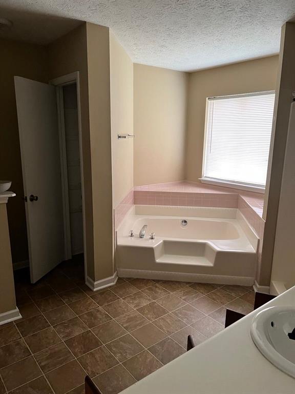 432 Manor Estates Dr, Stockbridge, GA 30281 - bathroom featuring a garden tub, tile patterned floors, baseboards, a textured ceiling, and vanity