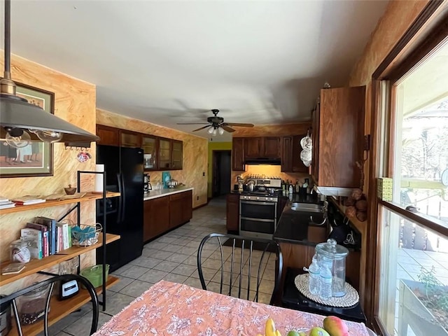 kitchen featuring stainless steel stove, sink, light tile patterned floors, black fridge, and dark brown cabinets