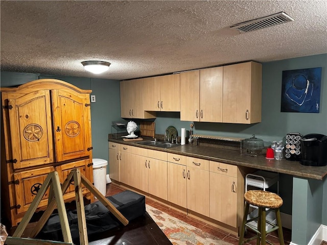 kitchen with sink, a kitchen breakfast bar, a textured ceiling, and light brown cabinets