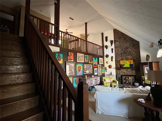 stairs with ceiling fan, a stone fireplace, and vaulted ceiling