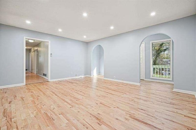 empty room with visible vents, baseboards, light wood finished floors, recessed lighting, and arched walkways