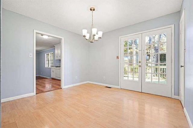 spare room featuring light wood-type flooring, visible vents, a notable chandelier, french doors, and baseboards