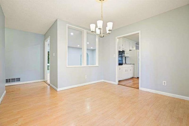 spare room with light wood-style flooring, a notable chandelier, baseboards, and visible vents