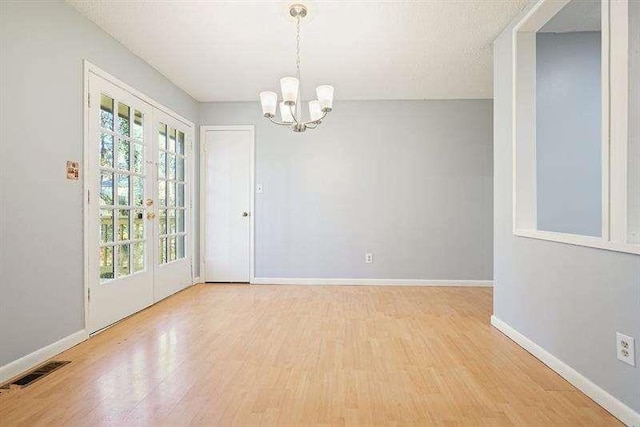 unfurnished room with visible vents, baseboards, french doors, wood finished floors, and a notable chandelier