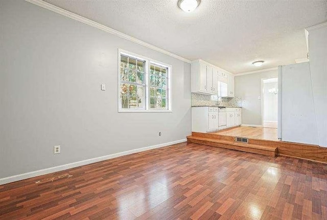 unfurnished living room featuring baseboards, light wood-style flooring, a sink, a textured ceiling, and crown molding