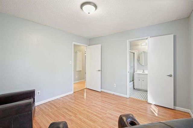 bedroom featuring light wood-style flooring, a textured ceiling, ensuite bathroom, and baseboards