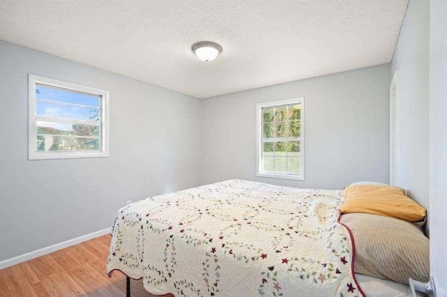 bedroom with a textured ceiling, baseboards, and light wood-style floors