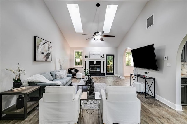 living area featuring arched walkways, light wood finished floors, visible vents, a glass covered fireplace, and ceiling fan