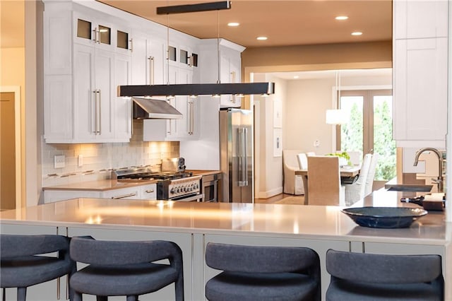 kitchen with white cabinets, appliances with stainless steel finishes, a kitchen breakfast bar, backsplash, and hanging light fixtures