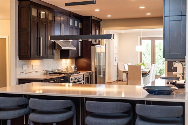 kitchen with a kitchen bar, extractor fan, decorative backsplash, and appliances with stainless steel finishes