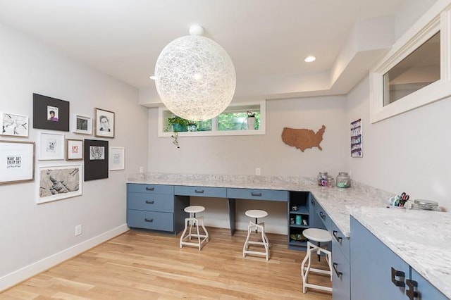 kitchen featuring blue cabinets, light wood-type flooring, and light stone countertops