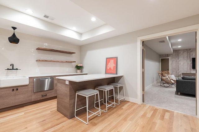 kitchen featuring kitchen peninsula, sink, light wood-type flooring, a tray ceiling, and a breakfast bar