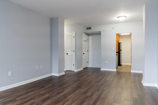 unfurnished room with dark wood-style floors, visible vents, and baseboards