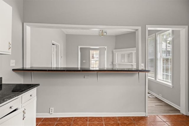 kitchen with a kitchen breakfast bar, dark stone counters, dark tile patterned flooring, and white cabinets