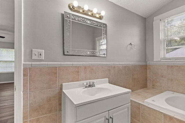 bathroom with vanity, a textured ceiling, ceiling fan, a relaxing tiled tub, and hardwood / wood-style floors