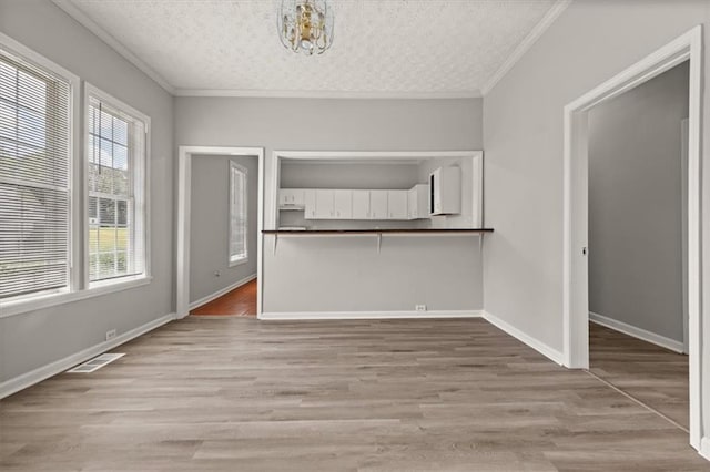 unfurnished dining area with a notable chandelier, a textured ceiling, hardwood / wood-style flooring, and crown molding