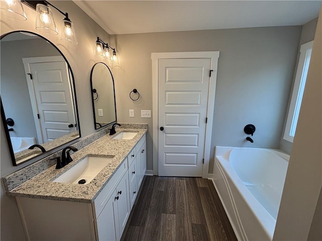 full bathroom featuring double vanity, wood finished floors, a bathing tub, and a sink