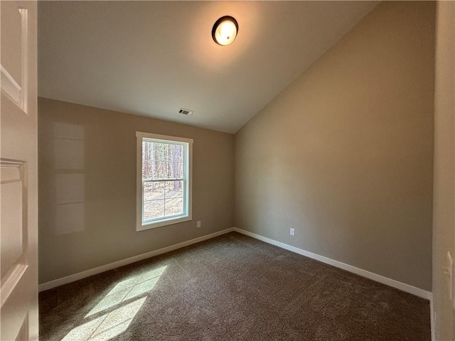 spare room featuring dark colored carpet, visible vents, lofted ceiling, and baseboards