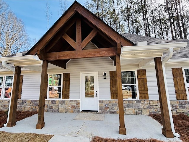 entrance to property with stone siding, covered porch, and roof with shingles