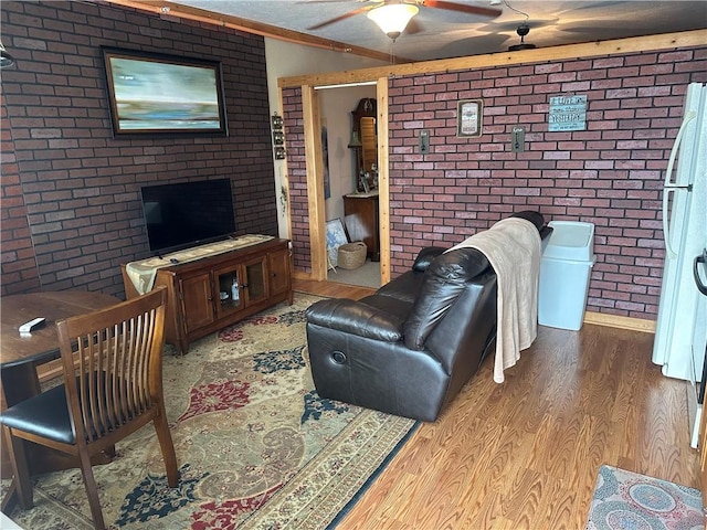 living room with ceiling fan, light hardwood / wood-style flooring, and brick wall