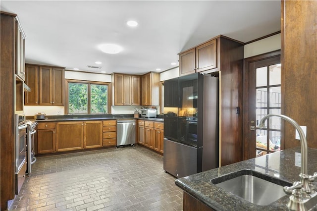 kitchen with dark stone counters, appliances with stainless steel finishes, a sink, and brick floor