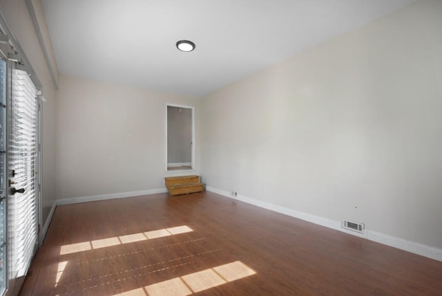 spare room with wood finished floors, visible vents, and baseboards