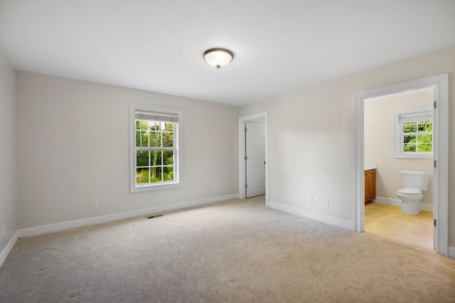 unfurnished bedroom with carpet, multiple windows, ensuite bath, and baseboards