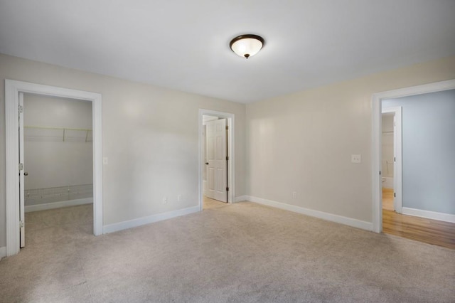 unfurnished bedroom with ensuite bathroom, light colored carpet, baseboards, a closet, and a walk in closet