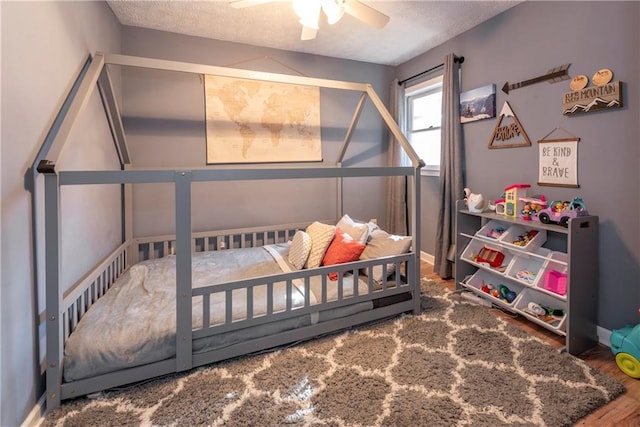 bedroom with ceiling fan, wood-type flooring, and a textured ceiling