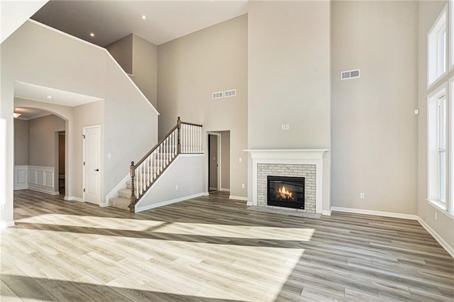 unfurnished living room with a towering ceiling, light hardwood / wood-style floors, and a brick fireplace