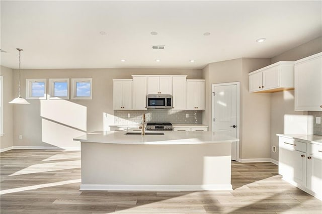 kitchen featuring hanging light fixtures, light wood-type flooring, white cabinets, and a kitchen island with sink