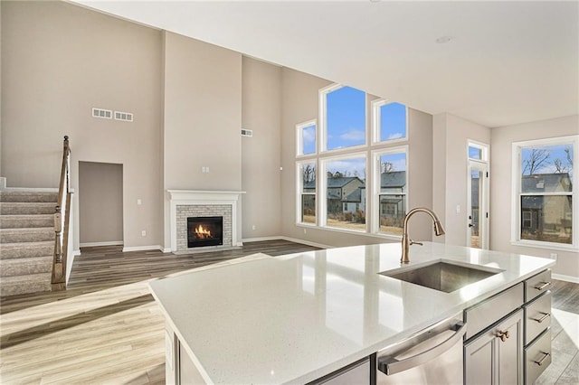 kitchen featuring a brick fireplace, stainless steel dishwasher, sink, a center island with sink, and light hardwood / wood-style flooring