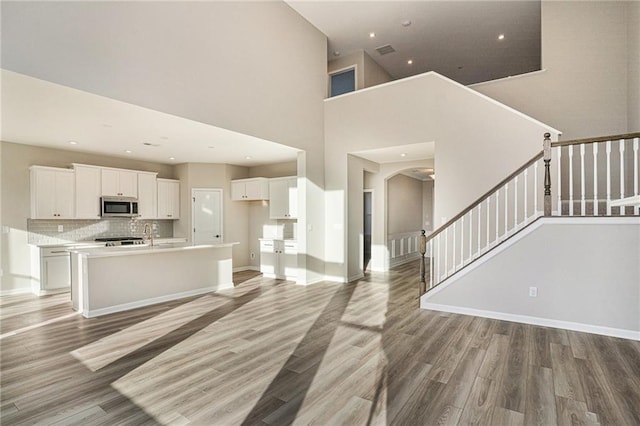 kitchen with a high ceiling, light hardwood / wood-style flooring, an island with sink, tasteful backsplash, and white cabinetry