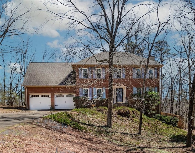 colonial house with aphalt driveway, a chimney, and an attached garage