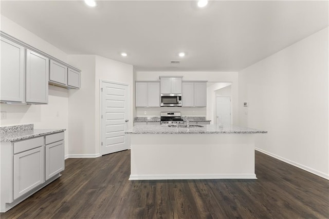 1278 Daurian Dr, Statham, GA 30666 - kitchen featuring appliances with stainless steel finishes, recessed lighting, a center island with sink, dark wood finished floors, and light stone counters