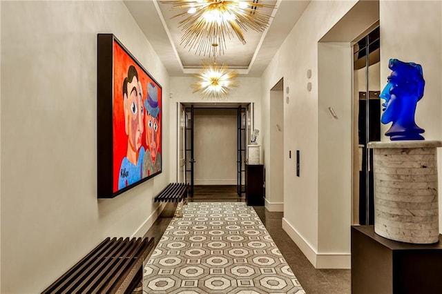 hall with a chandelier, a raised ceiling, and baseboards