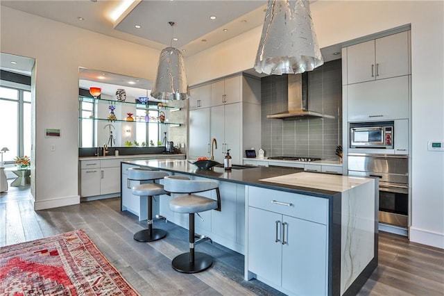 kitchen with wall chimney range hood, tasteful backsplash, stainless steel appliances, and dark wood-style flooring