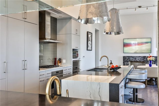 kitchen featuring tasteful backsplash, wall chimney exhaust hood, modern cabinets, appliances with stainless steel finishes, and a sink