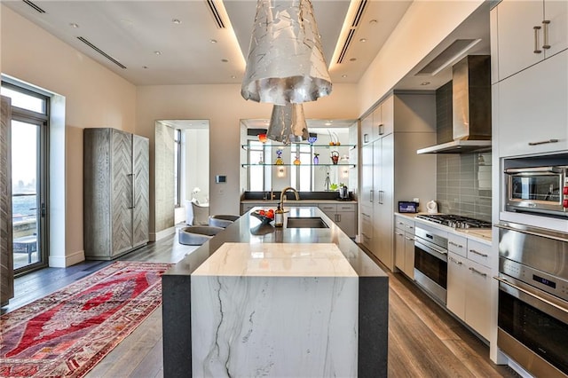 kitchen featuring dark wood finished floors, appliances with stainless steel finishes, a sink, modern cabinets, and wall chimney exhaust hood