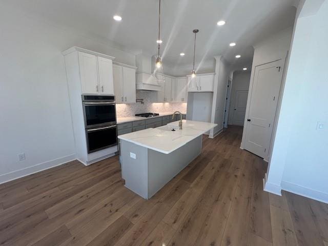 kitchen with backsplash, a center island with sink, hanging light fixtures, double oven, and white cabinetry