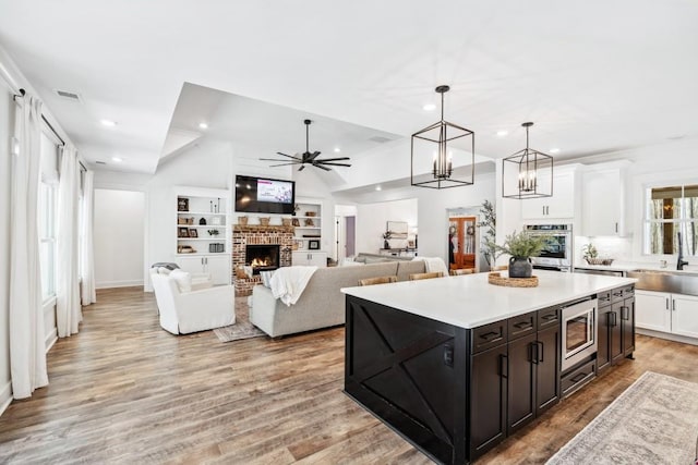 kitchen featuring a brick fireplace, appliances with stainless steel finishes, white cabinets, and a kitchen island